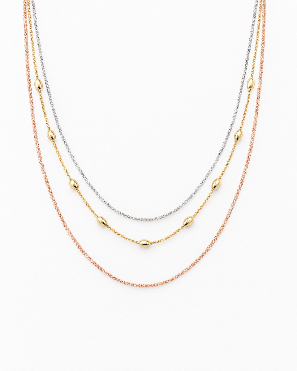 The layered necklace with three strands in silver, gold and rose tones and polished oval details, on a light background