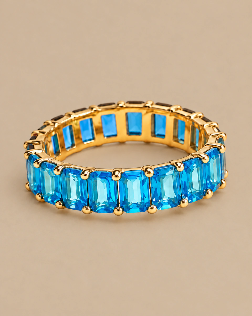The blue ring with rectangular stones and an open gold-tone setting, on a warm beige background