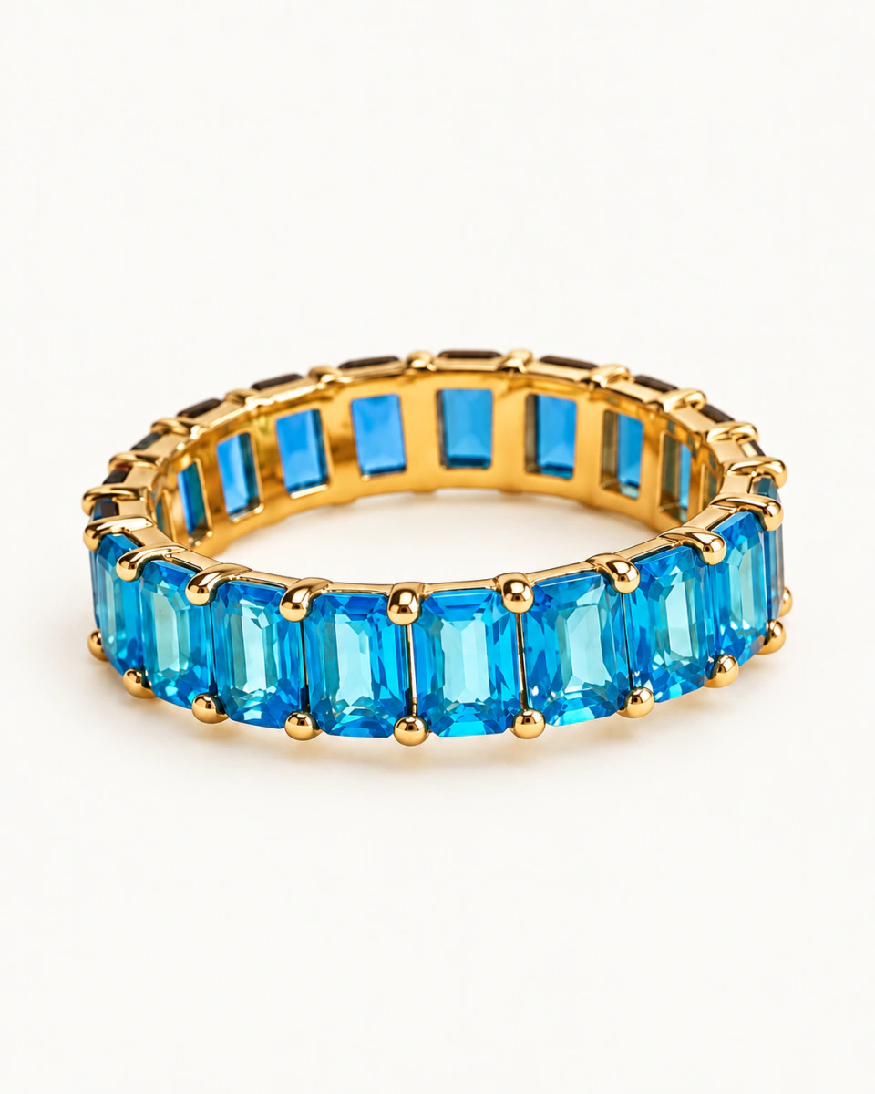 The blue ring with bright blue rectangular stones and small gold-tone prongs, on a light background