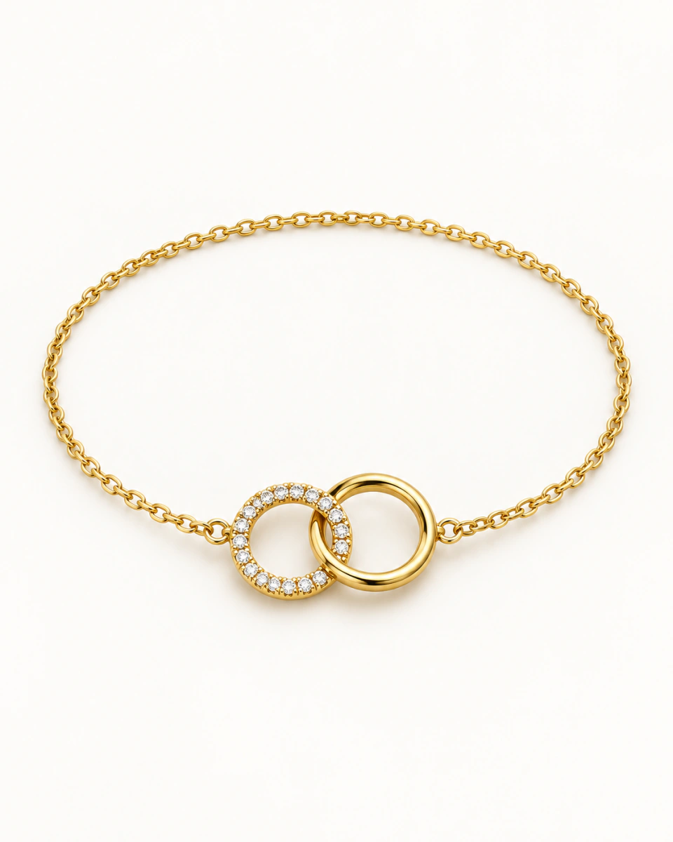 The gold-tone circle bracelet with two interlocked circles, one smooth and one set with clear stones, on a light background