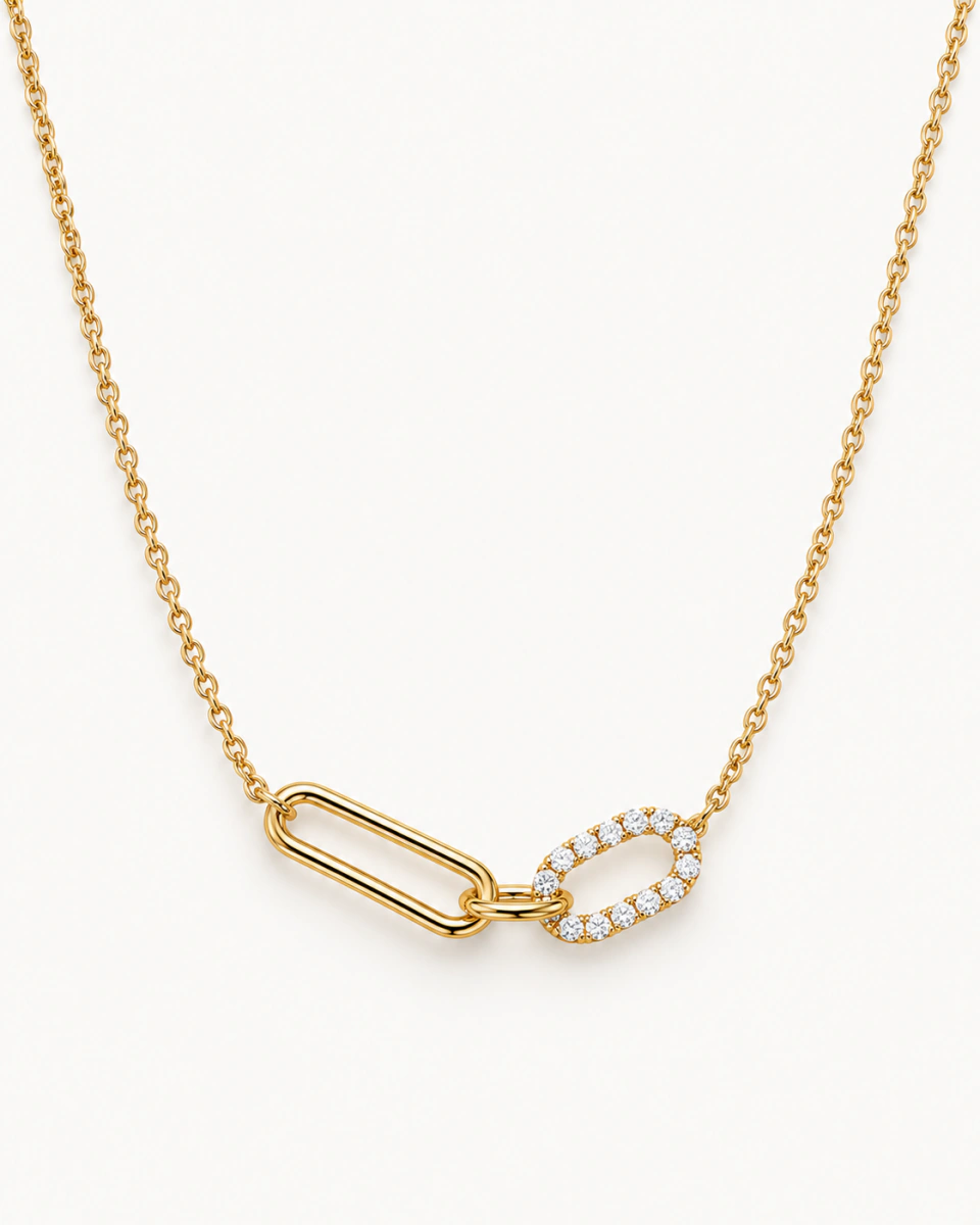 The oval-link necklace with an elongated gold-tone link joined to a clear-stone oval, on a light background