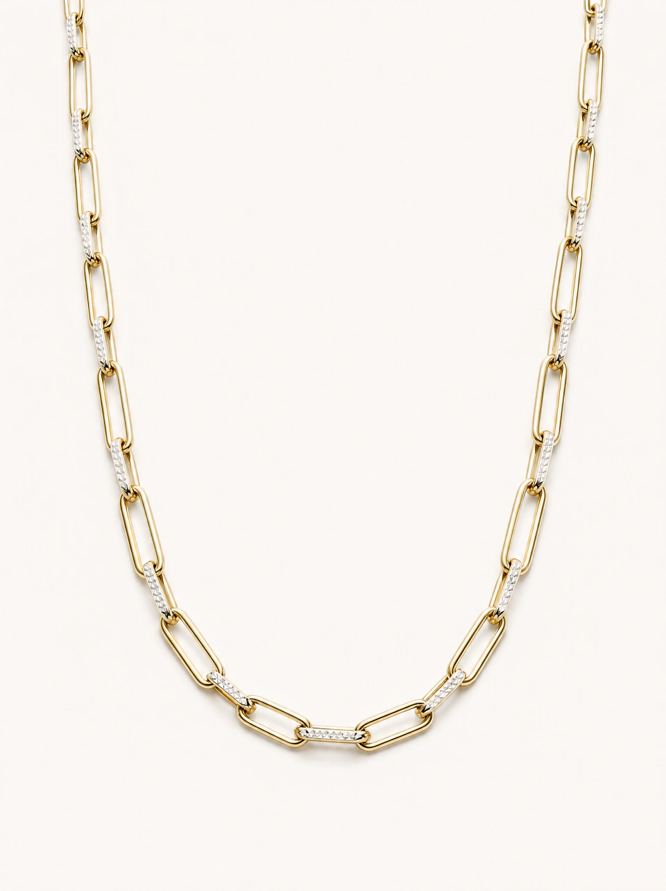 The paperclip necklace with long and short gold-tone links and finely textured metal details, on a light background