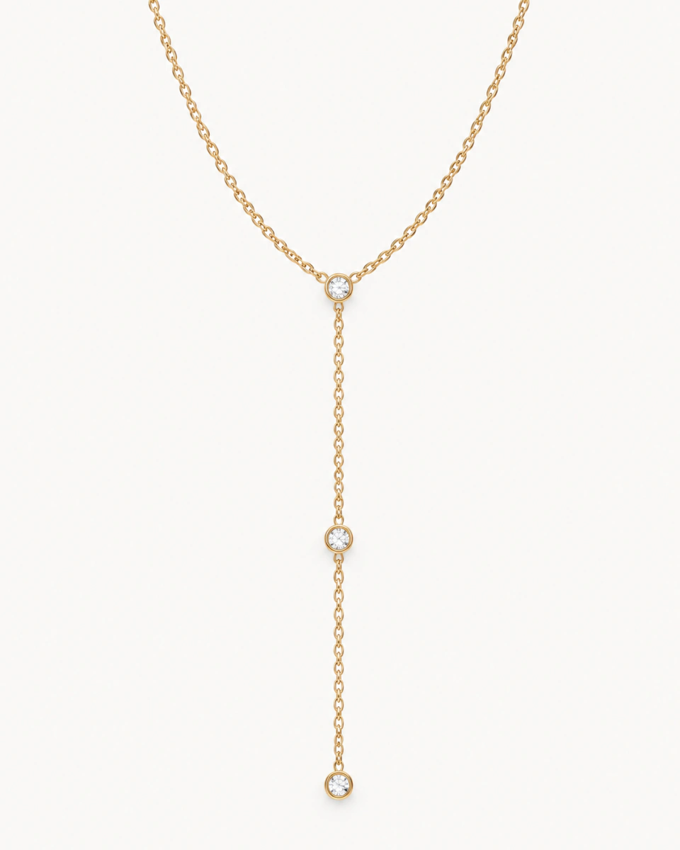 The three-stone lariat with three round clear stones in gold-tone bezels along a fine Y chain, on a light background