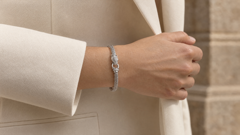 The silver-tone dragon bracelet worn on a wrist beside an ivory sleeve